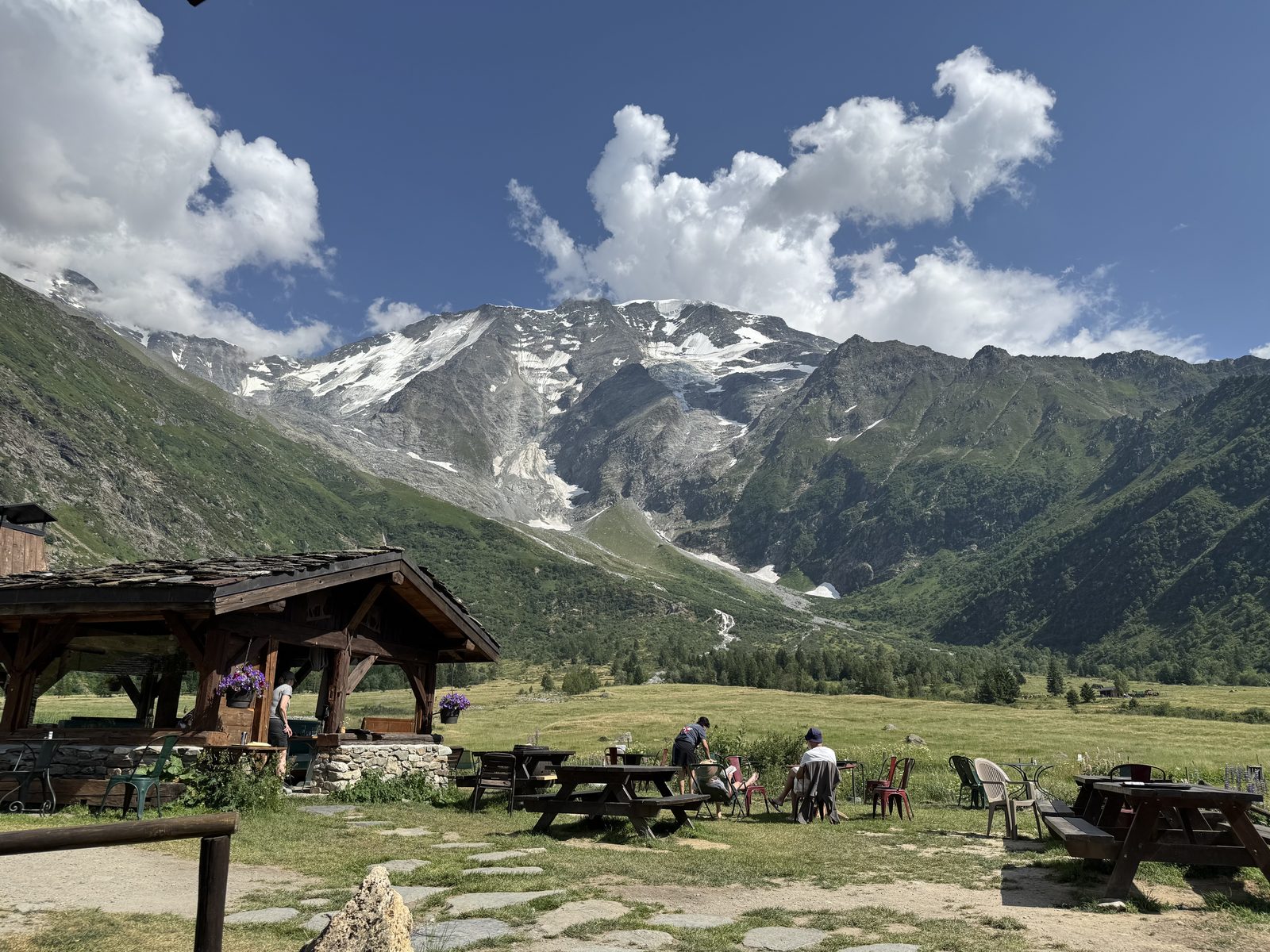 An alpine hut on a grassy slope with mountains behind it