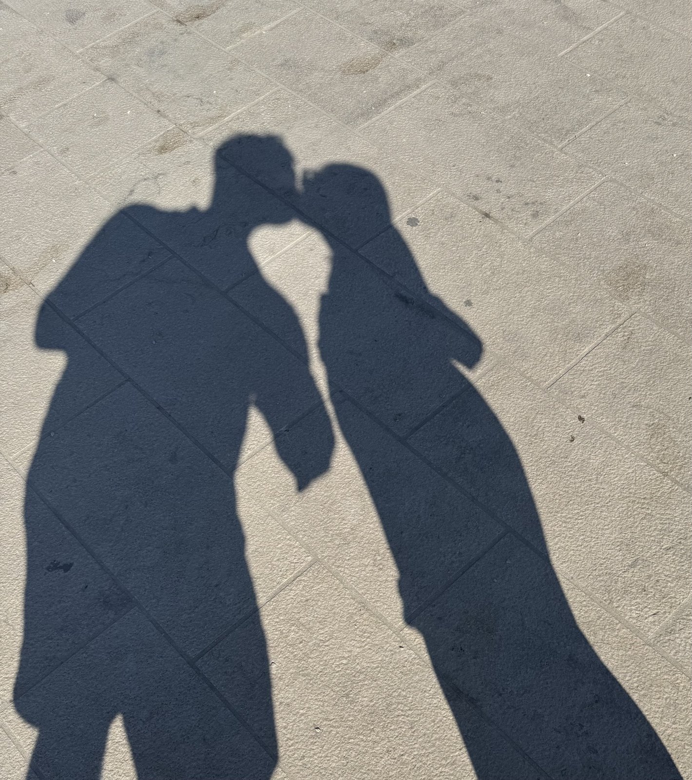 Shadows of a couple kissing on stone pavement