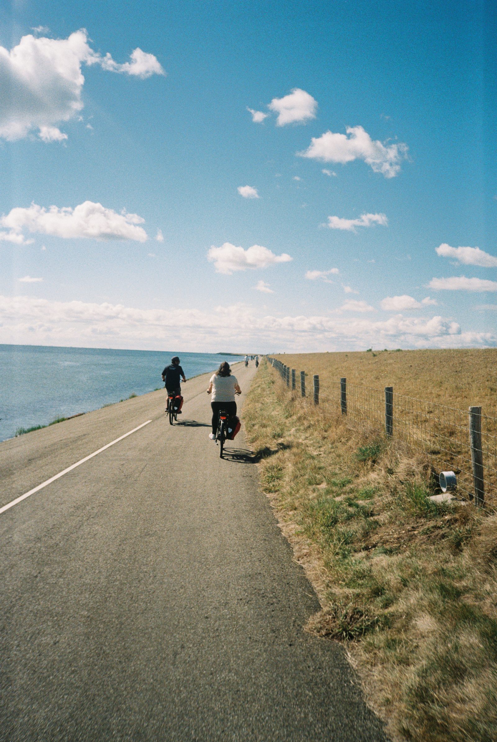 Two cyclists riding away along a coastal dyke beside the sea